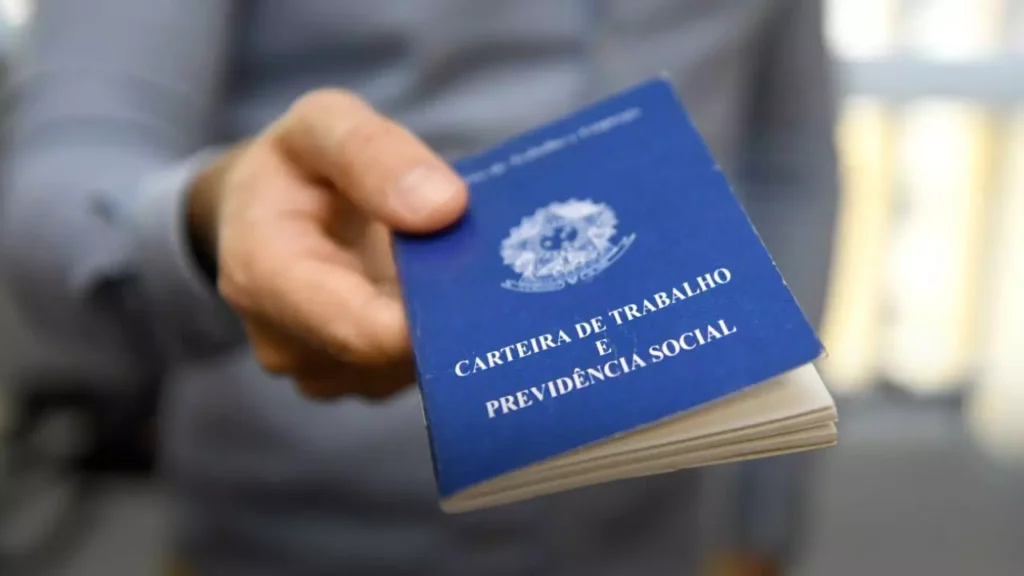 A imagem mostra uma pessoa segurando uma Carteira de Trabalho e Previdência Social (CTPS) do Brasil, que é um documento oficial utilizado para registrar o histórico profissional de um trabalhador.