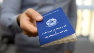 A imagem mostra uma pessoa segurando uma Carteira de Trabalho e Previdência Social (CTPS) do Brasil, que é um documento oficial utilizado para registrar o histórico profissional de um trabalhador.